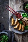 Gyozas aux haricots verts et sauce soja aux graines de sésame placés avec des baguettes près des bols avec des épices et des gousses de pois — Photo de stock