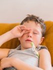 Сверху больной мальчик измеряет температуру с помощью электронного термометра, лежа дома на диване и болея гриппом — стоковое фото