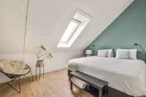 Комфортне ліжко з подушками, розташованими біля вікна в світлій горищній спальні в сучасному будинку — стокове фото