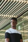 Confident African American male in casual t shirt standing in modern building and looking away — Stock Photo