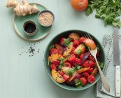 Vista superior de una ensalada de tomate crudo con fruta en una mesa con mantel verde rodeado de ingredientes saludables - foto de stock