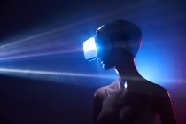 Maniquí de mujer en gafas VR futuristas colocadas bajo proyección brillante en habitación tenue - foto de stock