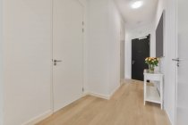 Corridoio con porta bianca chiusa e vaso di vetro con mazzo di fiori in leggero appartamento moderno con porta d'ingresso nera — Foto stock