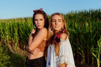 Zwei süße Freundinnen in Sommerkleidung schauen an einem sonnigen Tag in der Nähe eines Maisfeldes weg — Stockfoto