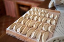 De arriba de las albóndigas de jiaozi tradicionales crudas servidas en la tabla de cortar de madera en la cocina - foto de stock