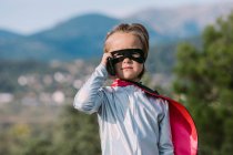 Self assured girl in eye mask superhero costume with cape having phone call on cellphone — Stock Photo