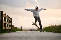 Ground level of full body of male in casual wear performing stunt on longboard on paved walkway — Stock Photo