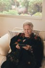 Konzentrierte Seniorin mit grauen Haaren ruht auf Couch und liest zu Hause im Wohnzimmer E-Book auf Tablet — Stockfoto