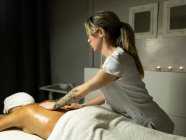 Massaggiatore femminile irriconoscibile che massaggia la schiena del cliente in asciugamano sul divano nel centro benessere leggero — Foto stock