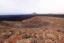 Picturesque view of crater of canic Caldereta against the mounts and sea under light sky in Lanzarote Canary Islands Spain — стокове фото