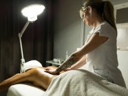 Massaggiatore femminile irriconoscibile che massaggia la schiena del cliente in asciugamano sul divano nel centro benessere leggero — Foto stock
