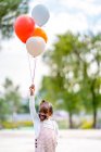 Alegre chica afroamericana con trenzas en ropa elegante corriendo con globos de colores en la mano en el parque durante el día - foto de stock
