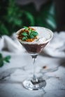 Glass of sweet mousse with chocolate and coconut garnished with mint leaves and placed on table with green plants — Stock Photo