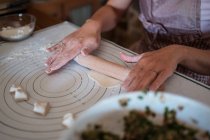 Зверху врожаю анонімної жінки в фартуху, що прокатує тісто на столі, готуючи пельмені з м'ясом на кухні — стокове фото