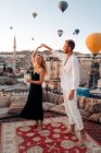 Corpo inteiro de casal descalço dançando juntos no terraço contra balões de ar quente voando no céu sem nuvens — Fotografia de Stock