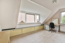 Interno di camera moderno con pannello su scrivania contro poltrona su parquet in soffitta di casa con finestre di giorno — Foto stock
