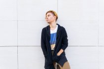 Serious young male in modern black cardigan looking into distance with thoughtful glance while standing near white wall on street — Stock Photo