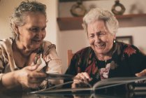 Irmãs idosas inspecionando fotos em álbum de fotos e discutindo memórias enquanto se sentam à mesa em casa juntas — Fotografia de Stock