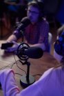 Concentrated young male and female colleagues in casual clothes and headphones sitting at table with microphones and communicating while recording podcast in modern studio — Stock Photo
