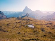 Terreno erboso con piccolo lago situato contro aspre montagne ripide contro cielo senza nuvole nella natura selvaggia della Spagna nei Pirenei — Foto stock