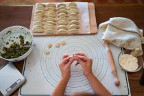 From above of crop anonymous female cook stuffing dough with meat while preparing traditional Chinese dumplings in kitchen — Stock Photo