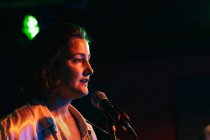 Впевнена леді з гітарним співом в мікрофоні під час виконання пісні в яскравому клубі — стокове фото