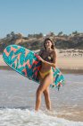 Vista lateral de surfista feminina esportiva com prancha de surf passeando em mar ondulado durante o treinamento em resort tropical no dia ensolarado — Fotografia de Stock