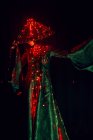 Нерозпізнавана загадкова жінка у творчому традиційному одязі та в'єтнамському головному уборі з червоним освітленням, що стоїть у темній студії на чорному тлі під час виступу. — стокове фото