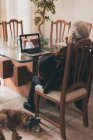 Vista posterior de una anciana irreconocible con el pelo gris corto sentada en la silla y escuchando el adiós de la hermana mientras hace una videollamada a través de netbook en casa - foto de stock