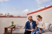 Hombre positivo abrazando a su novia mientras está sentado en un cómodo sofá y mirándose con sonrisas de dientes - foto de stock