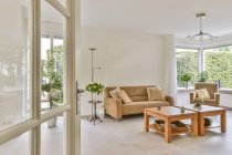 Интерьер современной гостиной с диваном и креслами с подушками в светлом доме — стоковое фото