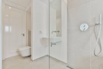 Évier installé sur le mur entre les toilettes et la cabine de douche en verre dans la salle de bain de style minimaliste léger — Photo de stock