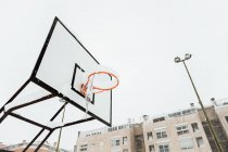 From below of hoop hanging on backboard on sports ground against residential buildings in winter day in Madrid — Stock Photo