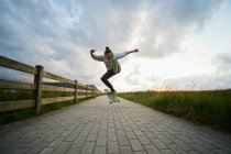 Ganzkörper-Männchen in Freizeitkleidung führen Stunt auf Longboard auf gepflastertem Gehweg aus — Stockfoto