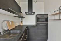 Design de cozinha minimalista moderna com armário de madeira prateleira pia com torneira e construído em eletrodomésticos e utensílios de cozinha e exaustor — Fotografia de Stock