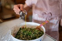From above of crop unrecognizable housewife in apron pouring olive oil into bowl with raw minced meat and herbs while preparing stuffing for jiaozi dumplings — Stock Photo