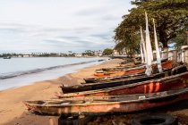 Fila di barche di legno invecchiate ormeggiate sulla spiaggia sabbiosa dell'oceano contro le piante tropicali verdi sull'isola So Tom e Prncipe nella giornata di sole — Foto stock