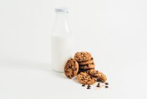 Pile of sweet crunchy cookies with chocolate chips placed on table with crumbs and milk on white background in room — Stock Photo