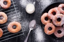 Süß gebratene Krapfen serviert auf einem Teller in der Nähe von Metall-Kühlregal und Krug Milch auf schwarz chaotisch Tisch mit Puderzucker — Stockfoto