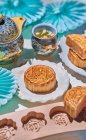 Сверху традиционные лунные пирожные с начинкой подаются на стол с выпечкой форм возле чайника с травяным чаем в светлом помещении — стоковое фото