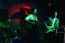 Homme jouant de la guitare tandis que la femme chantant et interprétant la chanson en club avec des néons — Photo de stock