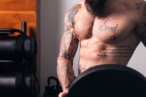 Ernte unkenntlich Sportler mit muskulösem Körper und nacktem Oberkörper steht mit schwerer Hantelscheibe in Turnhalle — Stockfoto