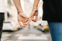 Visão traseira da colheita casal romântico irreconhecível segurando pequenos dedos enquanto caminhava na rua no dia ensolarado na cidade — Fotografia de Stock