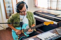 High angle of male musician in headphones playing electric guitar near microphone in recording studio — Stock Photo