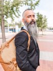 Вид збоку серйозного бородатого чоловіка в офіційному вбранні стоїть на камеру біля дороги на вулиці з сучасними будівлями — стокове фото