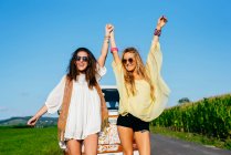 Dos hermosas y felices chicas caucásicas vestidas con ropa de verano de pie en la carretera fuera de una furgoneta - foto de stock