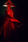 Unerkennbare Frau mit Maske in kreativem traditionellem Outfit und vietnamesischer Kopfbedeckung mit roter Beleuchtung im dunklen Studio auf schwarzem Hintergrund während des Auftritts — Stockfoto