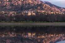 Ciudad costera con casas y edificio histórico situado cerca de la montaña ladera y todavía mar en el día de verano en la naturaleza en Castillo de Manzanares el Real en Madrid, España - foto de stock
