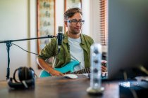 Мужчина-музыкант играет на электрогитаре возле микрофона в студии звукозаписи — стоковое фото
