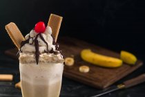 Verre de milkshake à la banane sucrée garni de gaufres à la crème fouettée et de cerise au chocolat sur le dessus — Photo de stock